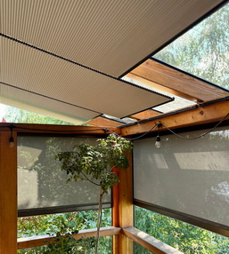 Outdoor patio or pergola with wooden beams and partially opened skylight panels letting in light, greenery visible outside safety screens