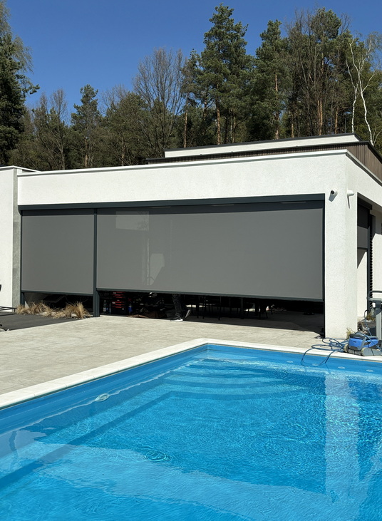 Modern white building with large gray retractable garage doors and a blue swimming pool in the foreground.