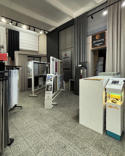 Showroom interior with metal display racks of curtain and blind samples near a white checkout counter.