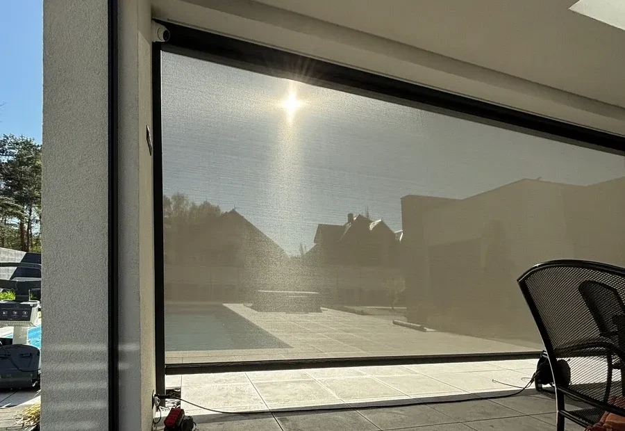 Sun light reflecting off a large glass door leading to a modern patio with a pool visible outside; a chair sits on the right.